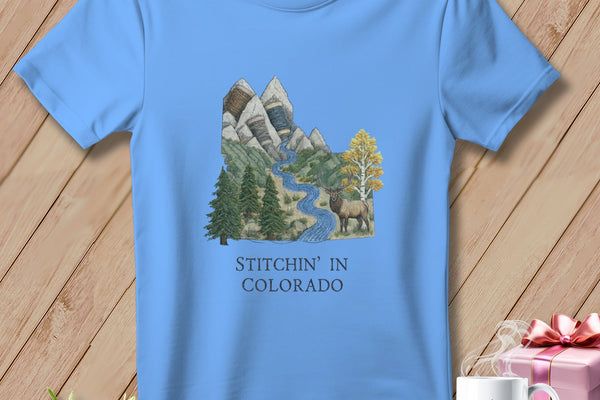 Light blue t-shirt with mountain landscape, elk, and text "Stitchin' in Colorado".