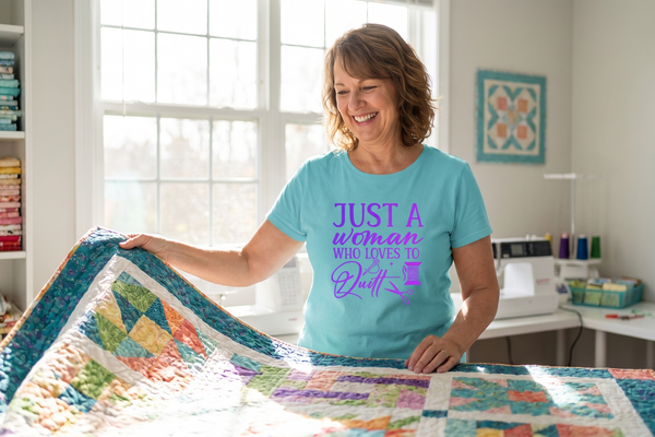 A smiling quilter unfolding a colorful patchwork quilt, wearing the Just A Woman Who Loves To Quilt premium tee