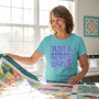 A smiling quilter unfolding a colorful patchwork quilt, wearing the Just A Woman Who Loves To Quilt premium tee