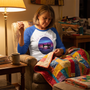 A quilter hand-stitching quilt binding by lamplight, wearing the Stitch Your Stress Away raglan tee
