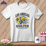 A white t-shirt hanging on a wooden background, featuring a blue and yellow ram graphic with text that reads Los Angeles Quilter.