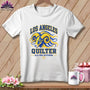 A white t-shirt hanging on a wooden background, featuring a blue and yellow ram graphic with text that reads Los Angeles Quilter.