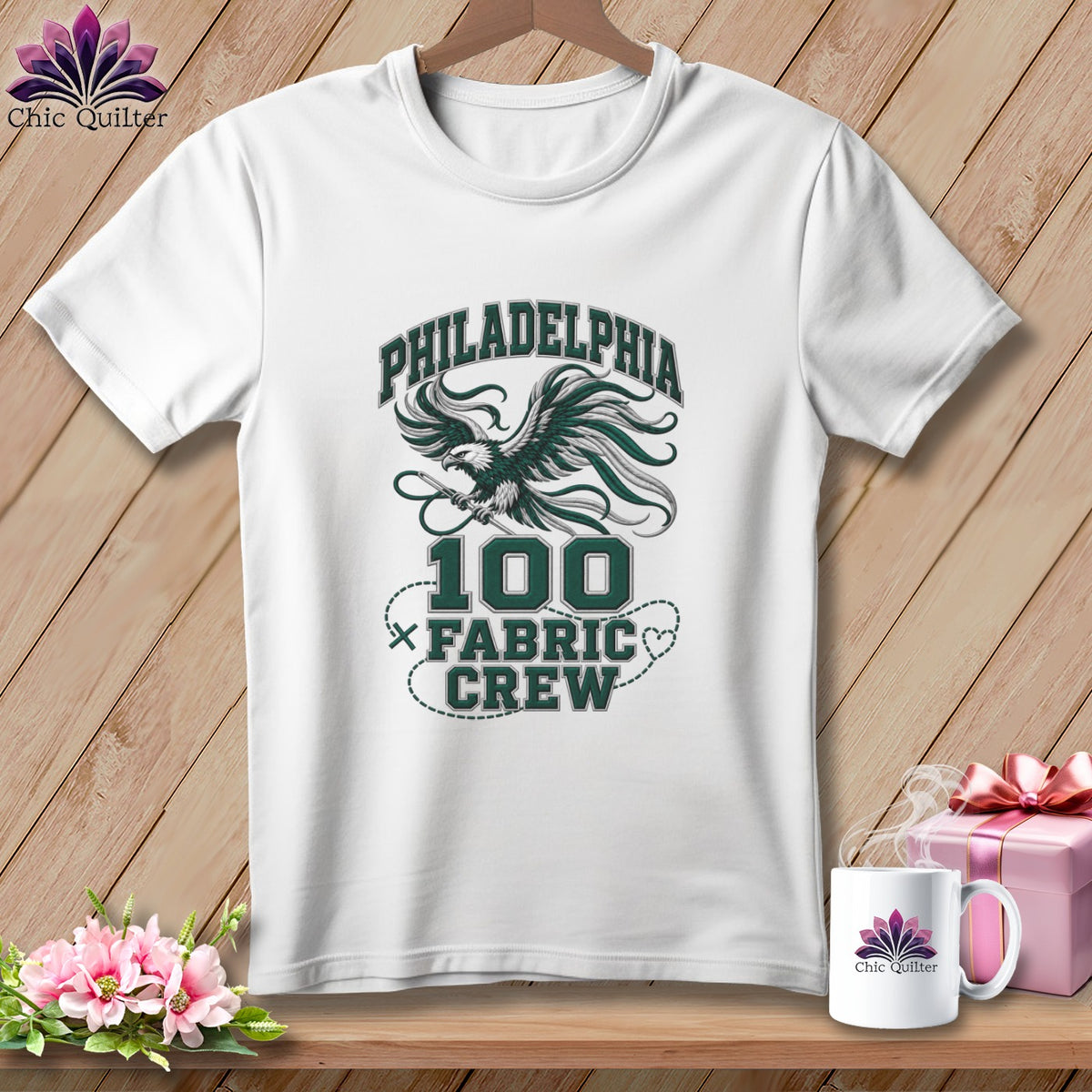 A white t-shirt on a wooden background features green text reading Philadelphia 100 Fabric Crew with an eagle graphic.