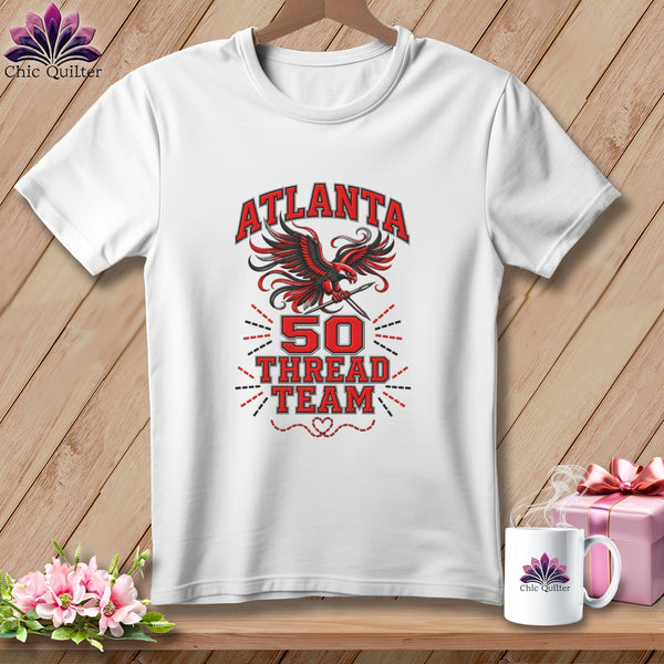 White t-shirt with a red and black Atlanta 50 Thread Team graphic on a wooden background.