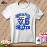 A white short-sleeved t-shirt on a wooden background, featuring a blue quilting graphic and the text Indianapolis Quilter Stitch Six.
