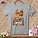 Chicken wearing a scarf sits on quilts with sewing supplies and text I'M WORKING ON IT.