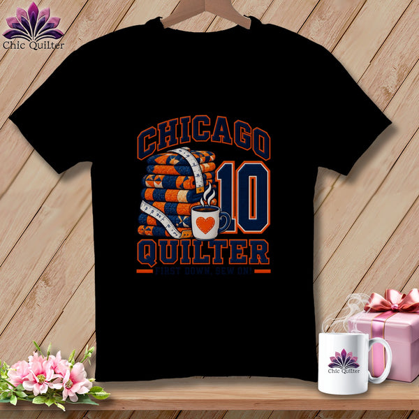 A black t-shirt features a graphic with a stack of quilts, a coffee mug, and text reading Chicago Quilter First Down, Sew On! and the number 10.