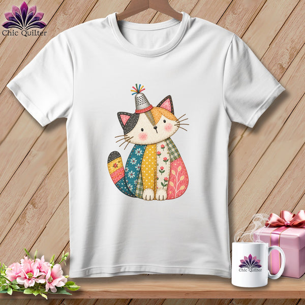 A white t-shirt features a colorful patchwork cat graphic wearing a thimble hat.