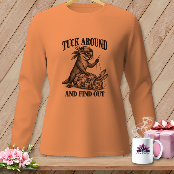An orange long-sleeve shirt displays a graphic of an otter sewing a quilt wrapped around a sweating rabbit, with the text TUCK AROUND AND FIND OUT.