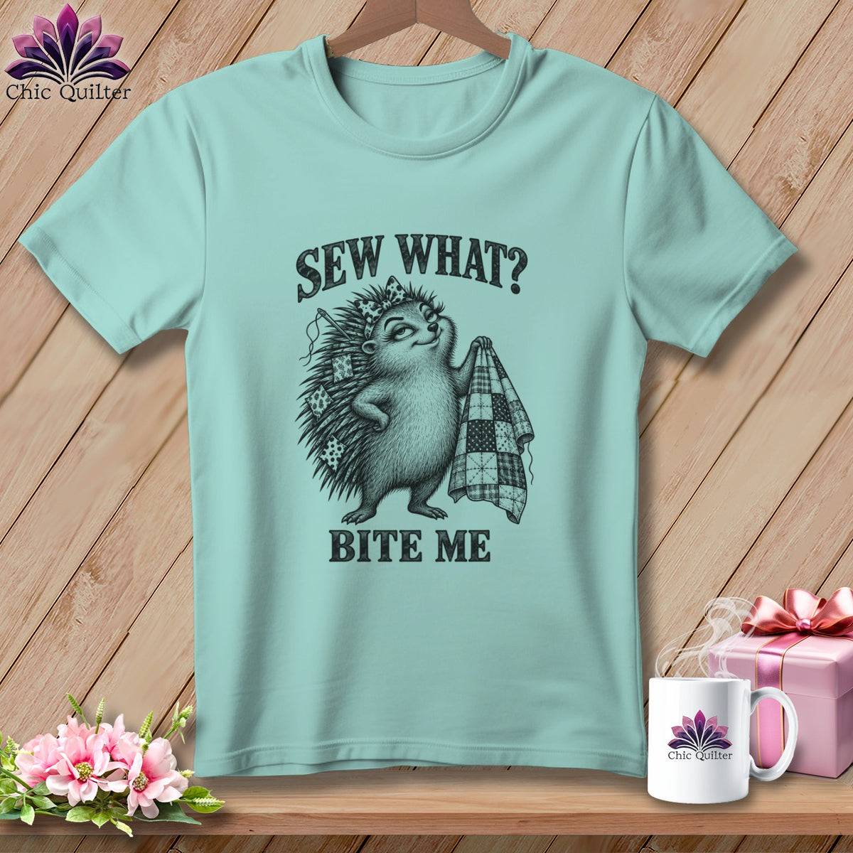 A light teal t-shirt featuring a hedgehog holding a quilt with text that reads Sew What Bite Me.