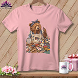 Pink t-shirt with graphic of tired bear sewing with fabric, thread, and sewing machine.