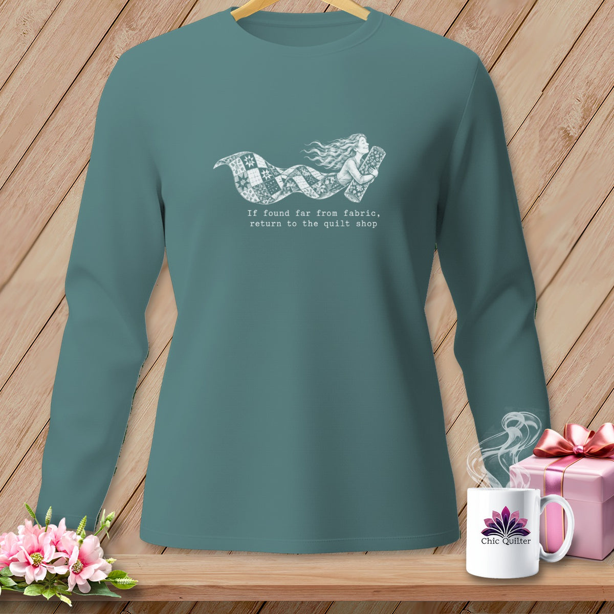 Teal long-sleeve shirt with a quilt design and text "If found far from fabric, return to the quilt shop".