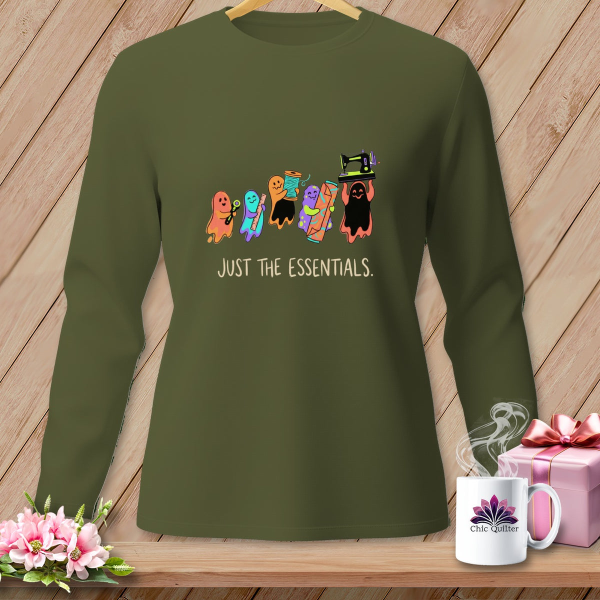 Olive green long-sleeve shirt with ghosts carrying sewing supplies and the text "JUST THE ESSENTIALS."