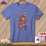A periwinkle t-shirt features a colorful, feathered bird in a basket with the text Scrappy & Happy.