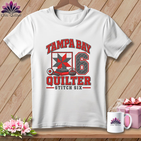 White crewneck t-shirt featuring a Tampa Bay Quilter graphic with a red quilt block, the number six, and sewing tools.