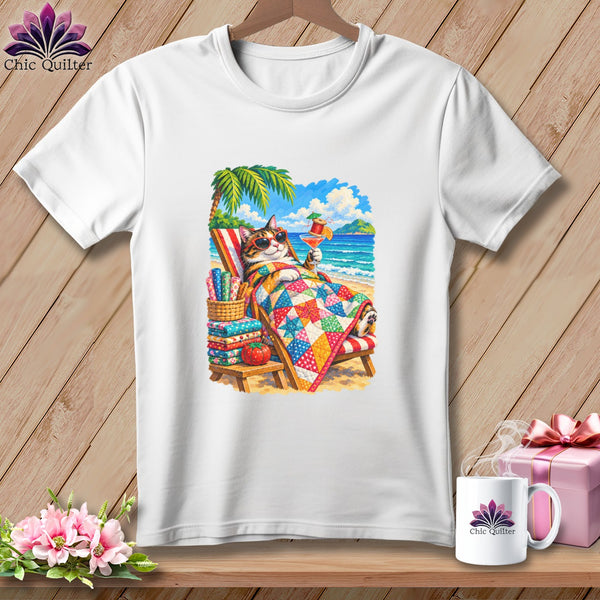 White t-shirt featuring a colorful graphic of a cat relaxing in a beach chair with a cocktail and quilt.