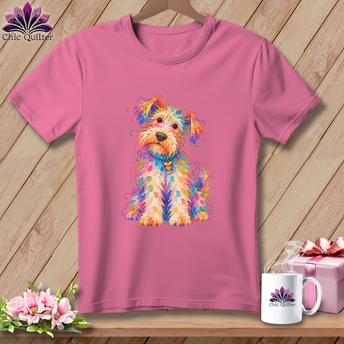 A pink t-shirt hangs on a wooden background, featuring a colorful watercolor illustration of a scruffy dog on the chest.