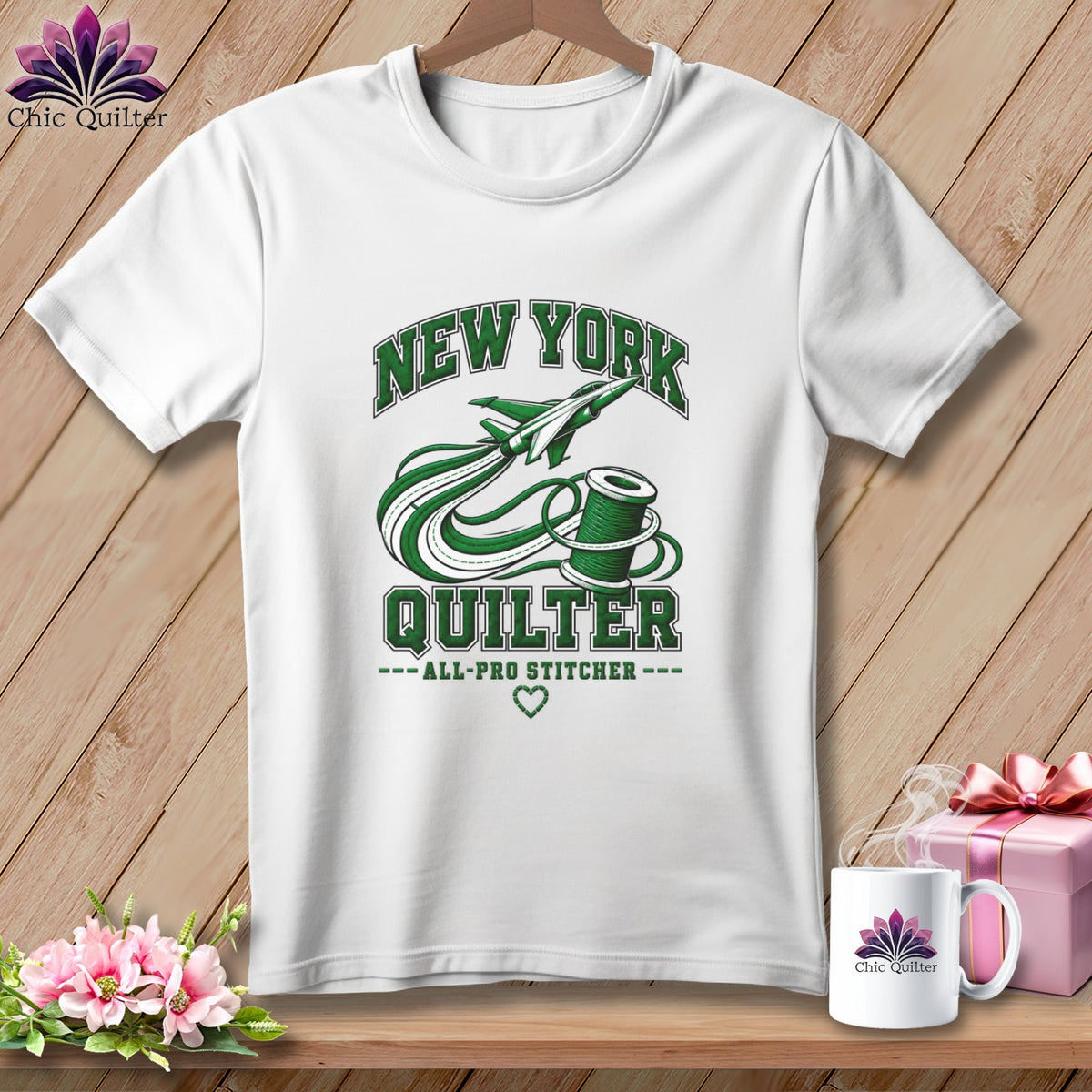 White t-shirt with a green graphic featuring a New York Quilter design, hanging against a wooden background.