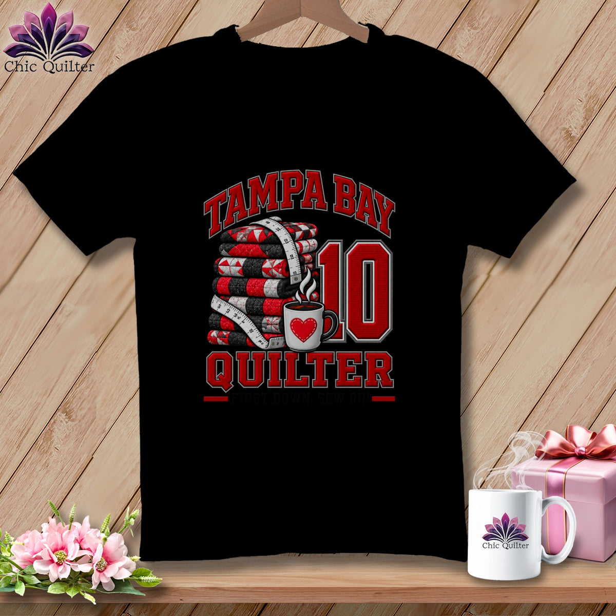 A black t-shirt features a graphic with a stack of quilts, a measuring tape, and a coffee mug with a red heart. Text reads Tampa Bay Quilter 10.