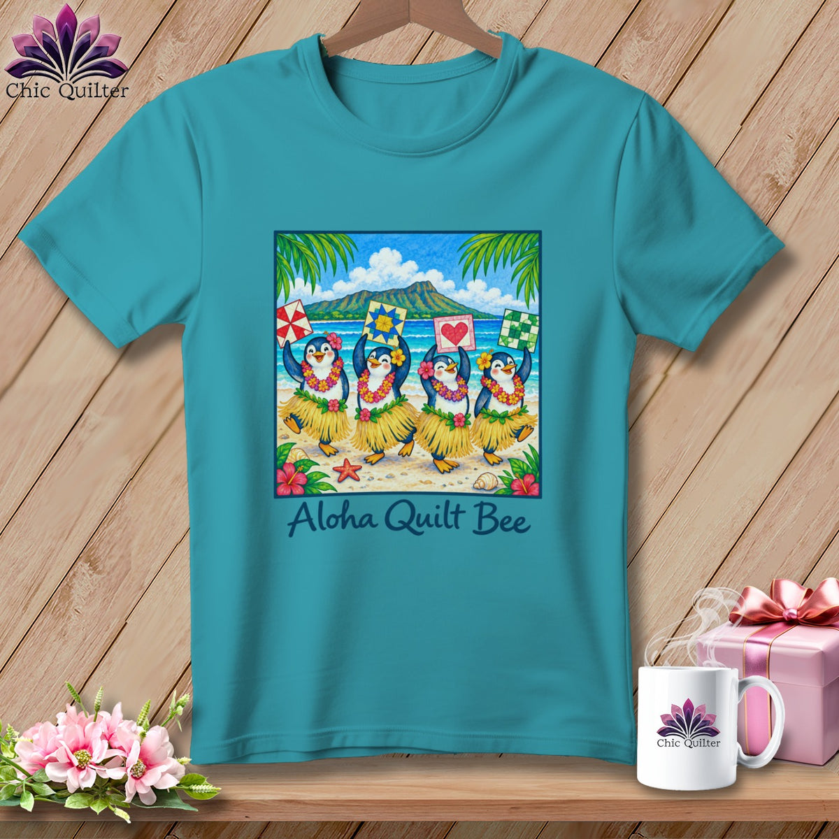 Teal t-shirt featuring a square graphic of hula-dancing penguins holding quilt blocks, with text reading Aloha Quilt Bee.