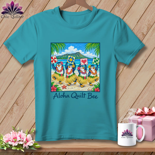 Teal t-shirt featuring a square graphic of hula-dancing penguins holding quilt blocks, with text reading Aloha Quilt Bee.