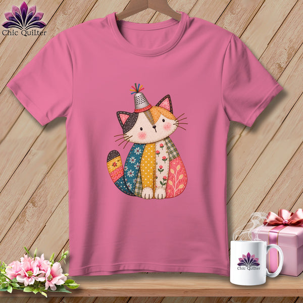 Pink t-shirt featuring a cute patchwork cat illustration wearing a thimble hat, displayed on wood.