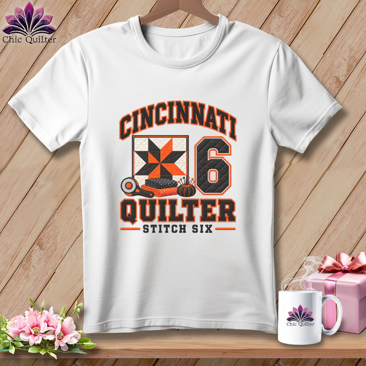 A white t-shirt features a Cincinnati Quilter graphic with a quilt square, number six, and sewing tools.