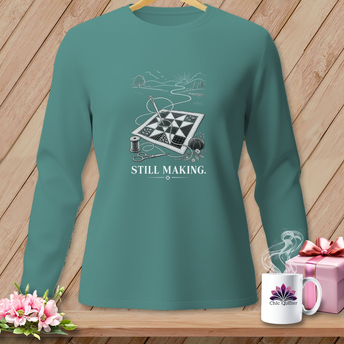 Teal long-sleeve shirt with a quilt, needle, thread, scissors, and text "STILL MAKING."