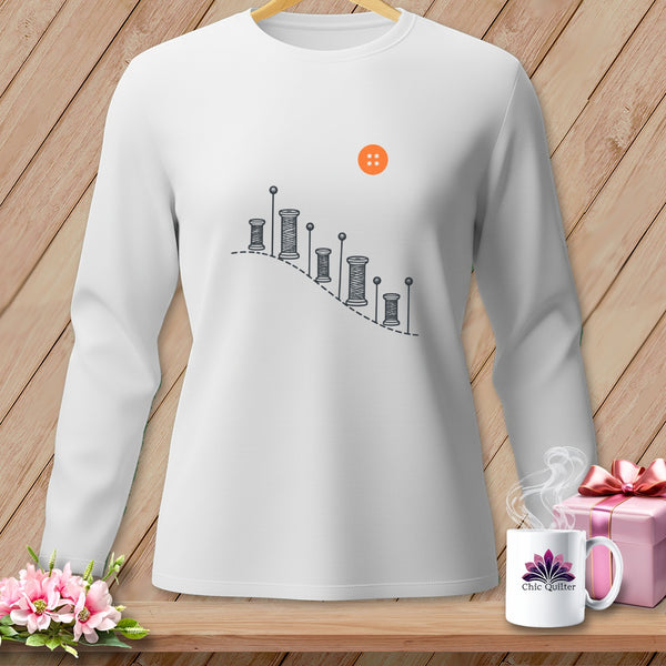 White long-sleeved shirt with sewing graphic and orange button detail.