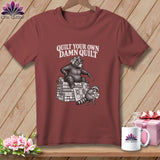 Maroon t-shirt featuring a black and white graphic of a bear and raccoon quilting, with text reading 
