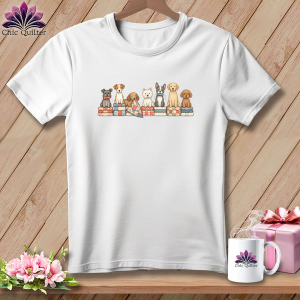 A white crewneck t-shirt features a central graphic of seven different dogs sitting on stacked quilts.