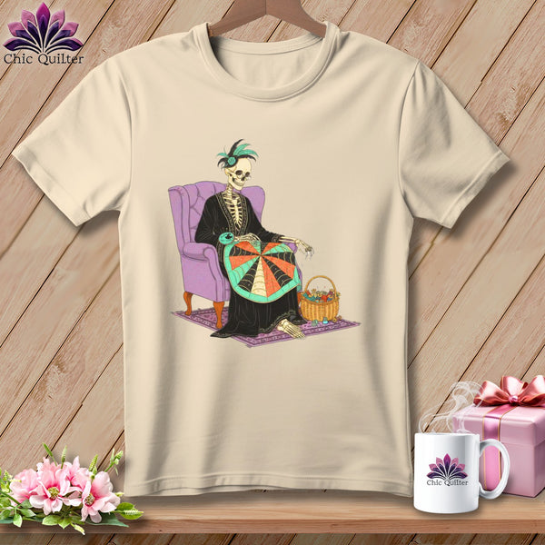 Skeleton quilter with yarn basket sits in purple chair, featured on cream t-shirt.