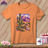 Orange t-shirt featuring a desert landscape graphic with a cactus, mountains, and a patterned quilt.