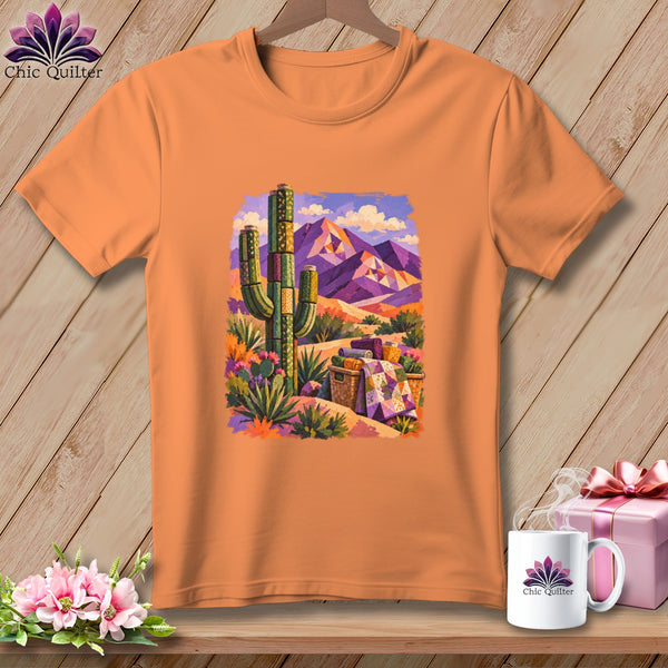 Orange t-shirt featuring a desert landscape graphic with a cactus, mountains, and a patterned quilt.