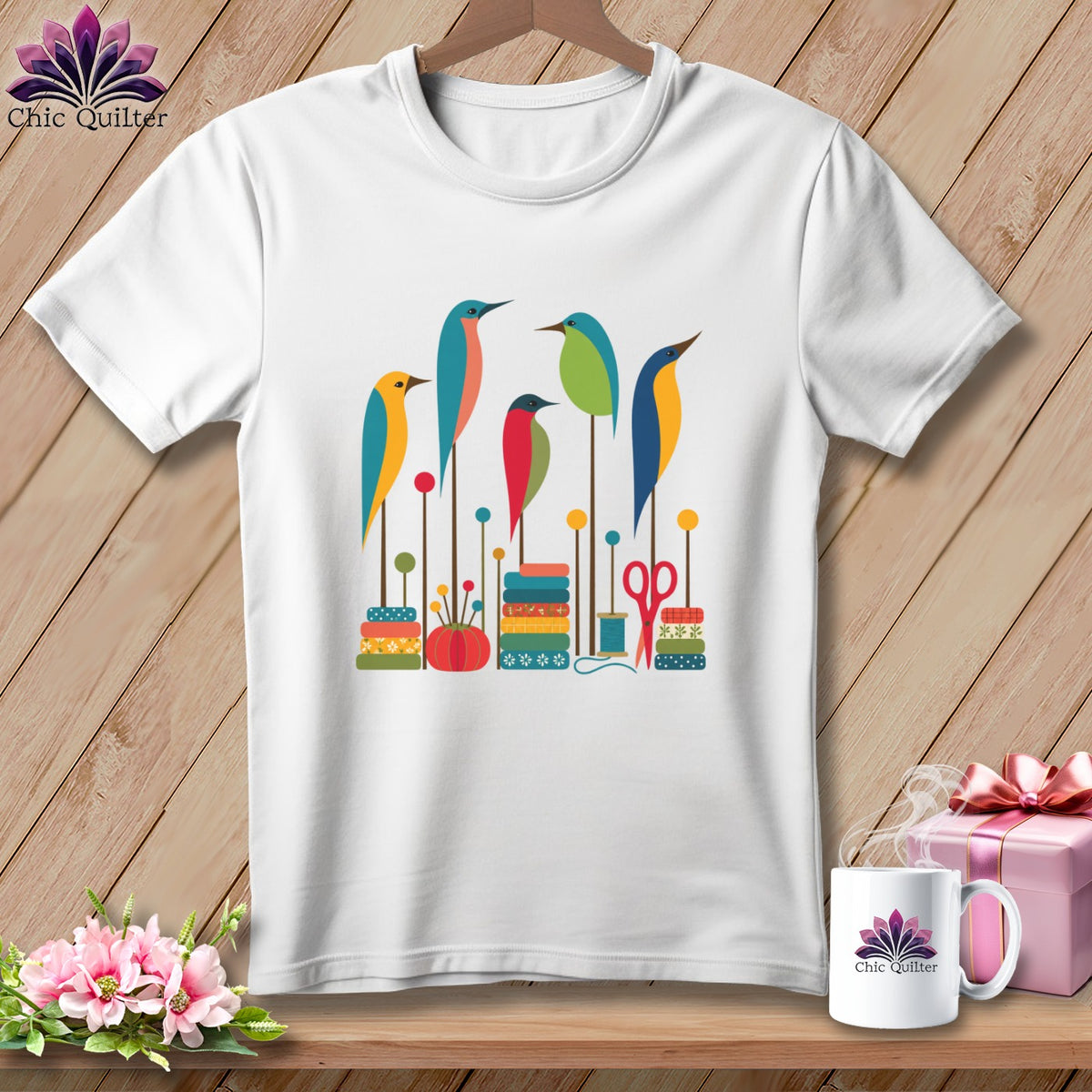 A white crewneck t-shirt featuring a colorful graphic of five stylized birds perched on sewing supplies.