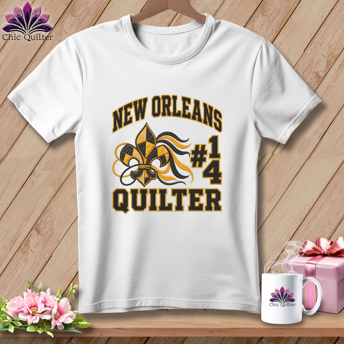 White t-shirt on a wooden hanger with New Orleans Quilter #14 graphic, next to a mug and pink gift box.