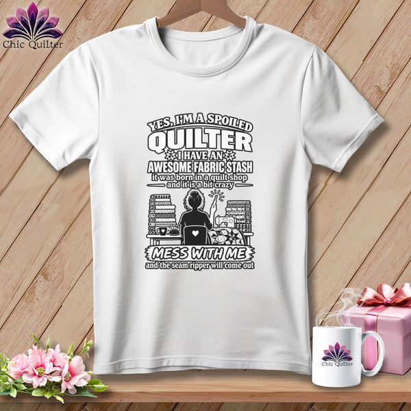 A white t-shirt featuring black text about quilting, with a silhouette of a quilter surrounded by fabric.