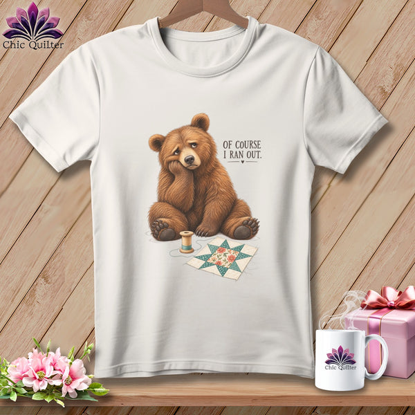 White t-shirt with a sad bear sitting next to a quilt square and thread.