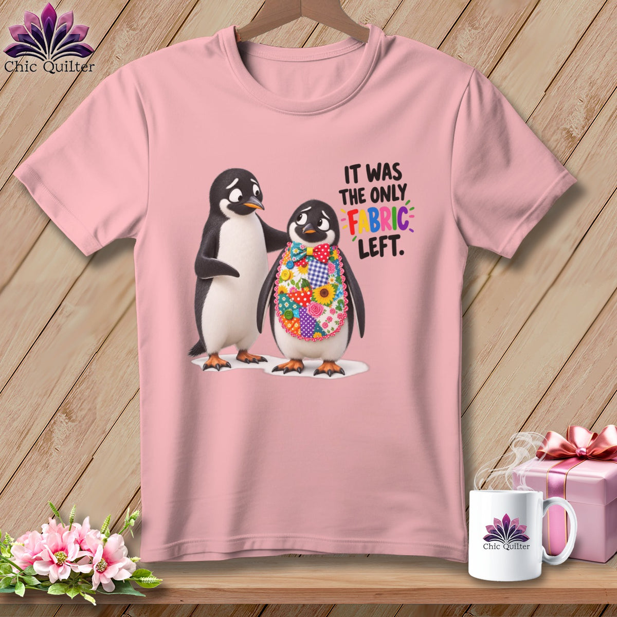 Pink t-shirt with two penguins, one wearing a colorful fabric bib. Text says "IT WAS THE ONLY FABRIC LEFT."