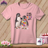 Pink t-shirt with two penguins, one wearing a colorful fabric bib. Text says 