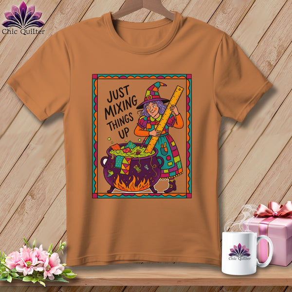 Brown t-shirt with a witch mixing fabric scraps in a cauldron and the text "Just Mixing Things Up".