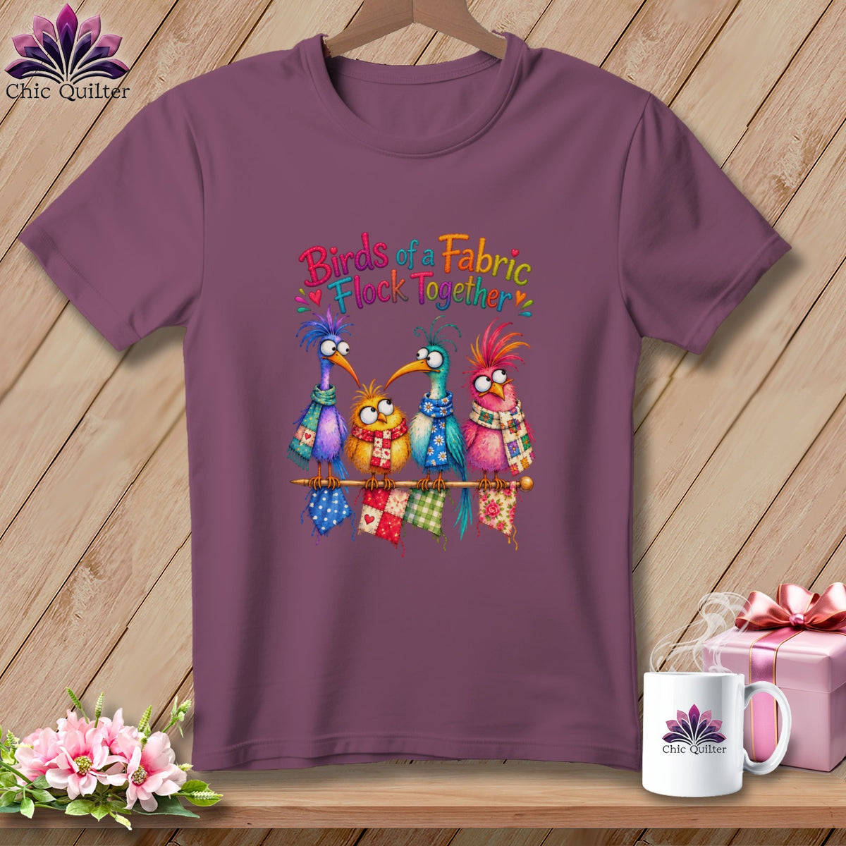 Plum t-shirt featuring four colorful, whimsical cartoon birds perched on a spool with the text Birds of a Fabric Flock Together.
