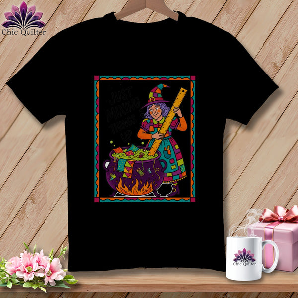 Black t-shirt with a witch stirring a cauldron, reading "Just Mixing Things Up".