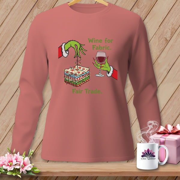 Pink long-sleeve shirt with Grinch-like hands, fabric stacks, wine glass, and text.
