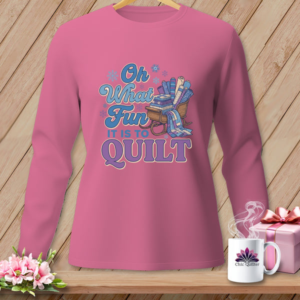Pink long sleeve shirt with "Oh What Fun It Is To Quilt" text and sled of fabric rolls.