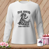 A white long-sleeved shirt features a graphic of an otter sewing a rabbit into a quilt, with text that reads 