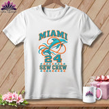 A white t-shirt hanging on a wooden background features a graphic with Miami, a dolphin, and the text Sew Crew.