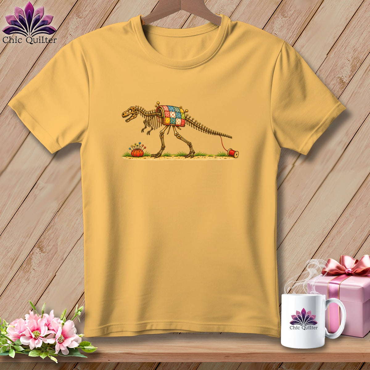A gold short-sleeve t-shirt with a graphic of a dinosaur skeleton wearing a quilt.