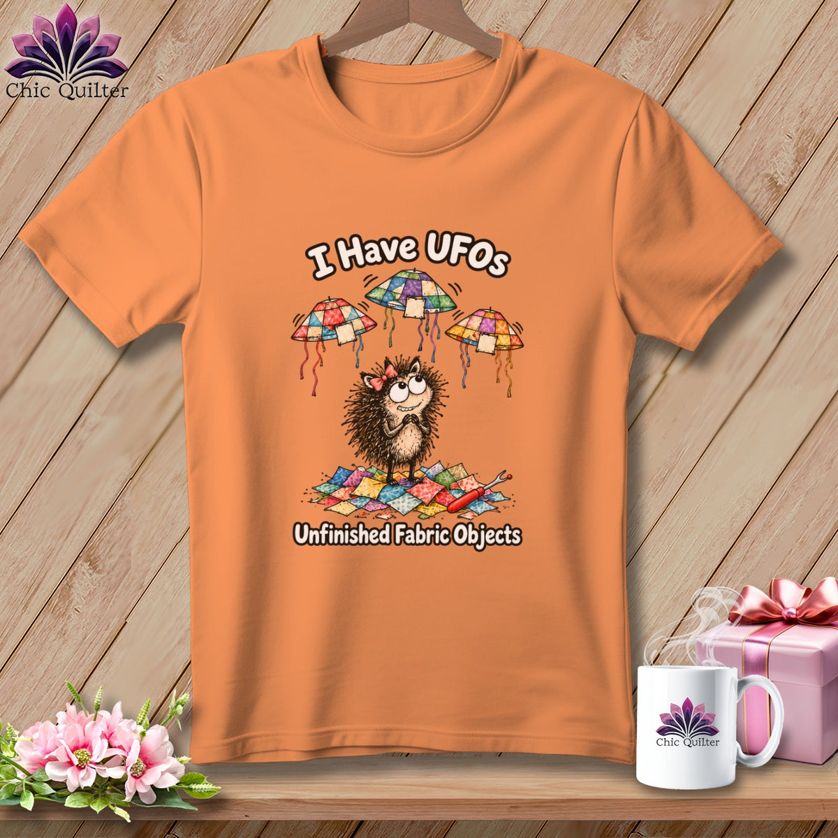 An orange t-shirt displays a cartoon hedgehog surrounded by quilting scraps and flying UFO-shaped patchwork quilts.