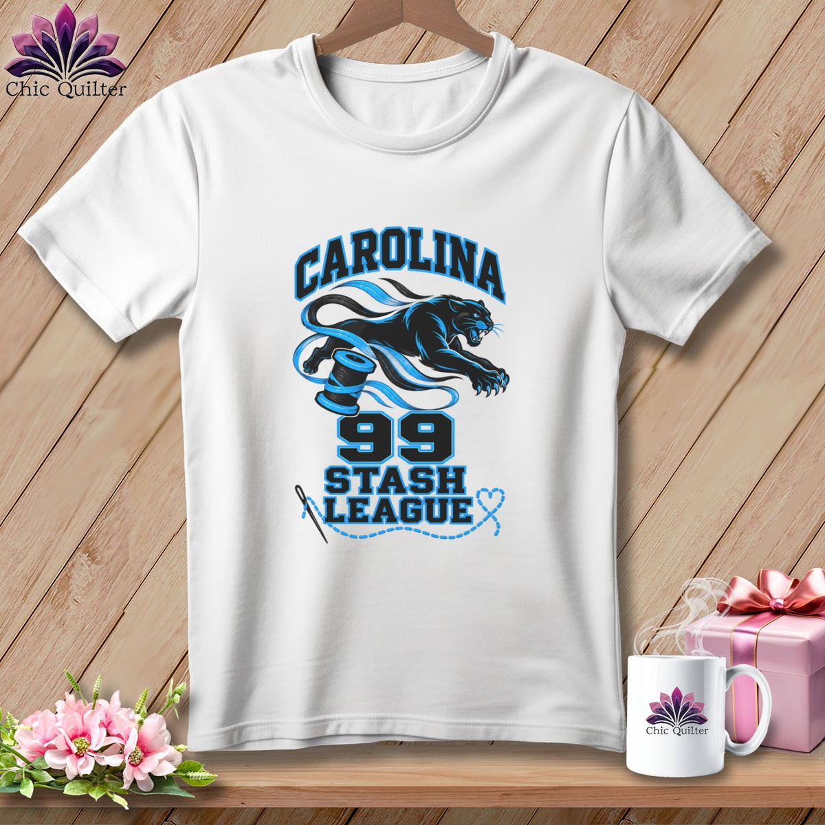 A white t-shirt hanging against a wooden background features a black panther, blue spools of thread, and the text Carolina 99 Stash League.
